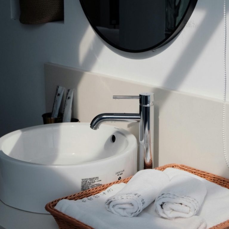 Modern bathroom sink with a chrome faucet and neatly rolled towels in a basket.
