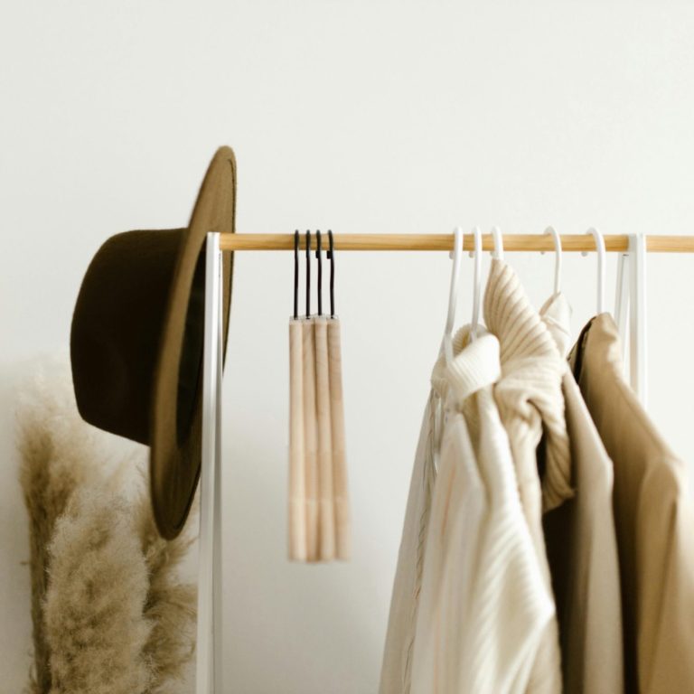 wardrobe reset services A hat and neutral-toned clothing hang on a wooden rail with a decorative touch.