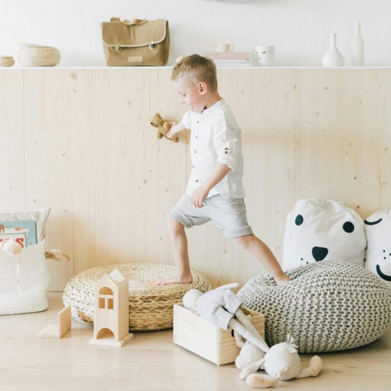 Child playing on soft furniture, holding a toy in a bright, minimalist room.