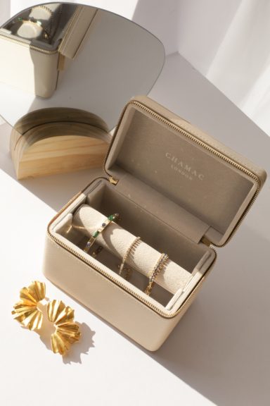 A beige jewellery box with gold accents, containing rings and a decorative hair accessory.